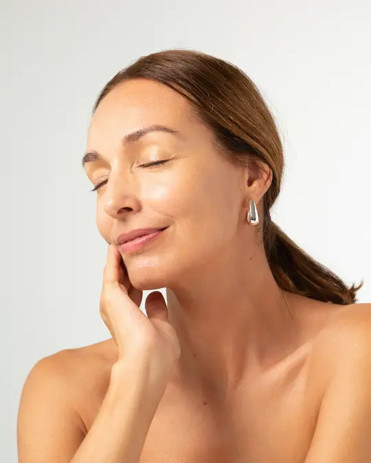 Piękna dojrzała kobieta, która lekko się uśmiecha i dotyka swojej twarzy